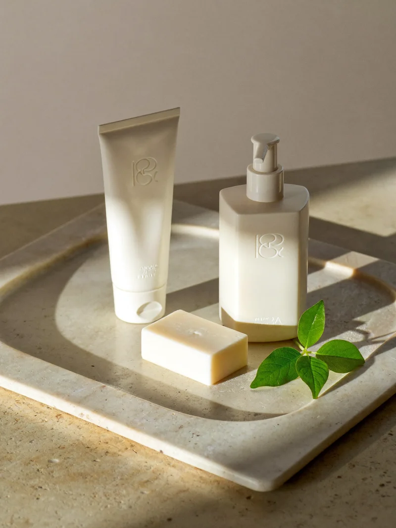 Crema mani, lozione corpo e sapone solido su un vassoio di pietra con foglie
